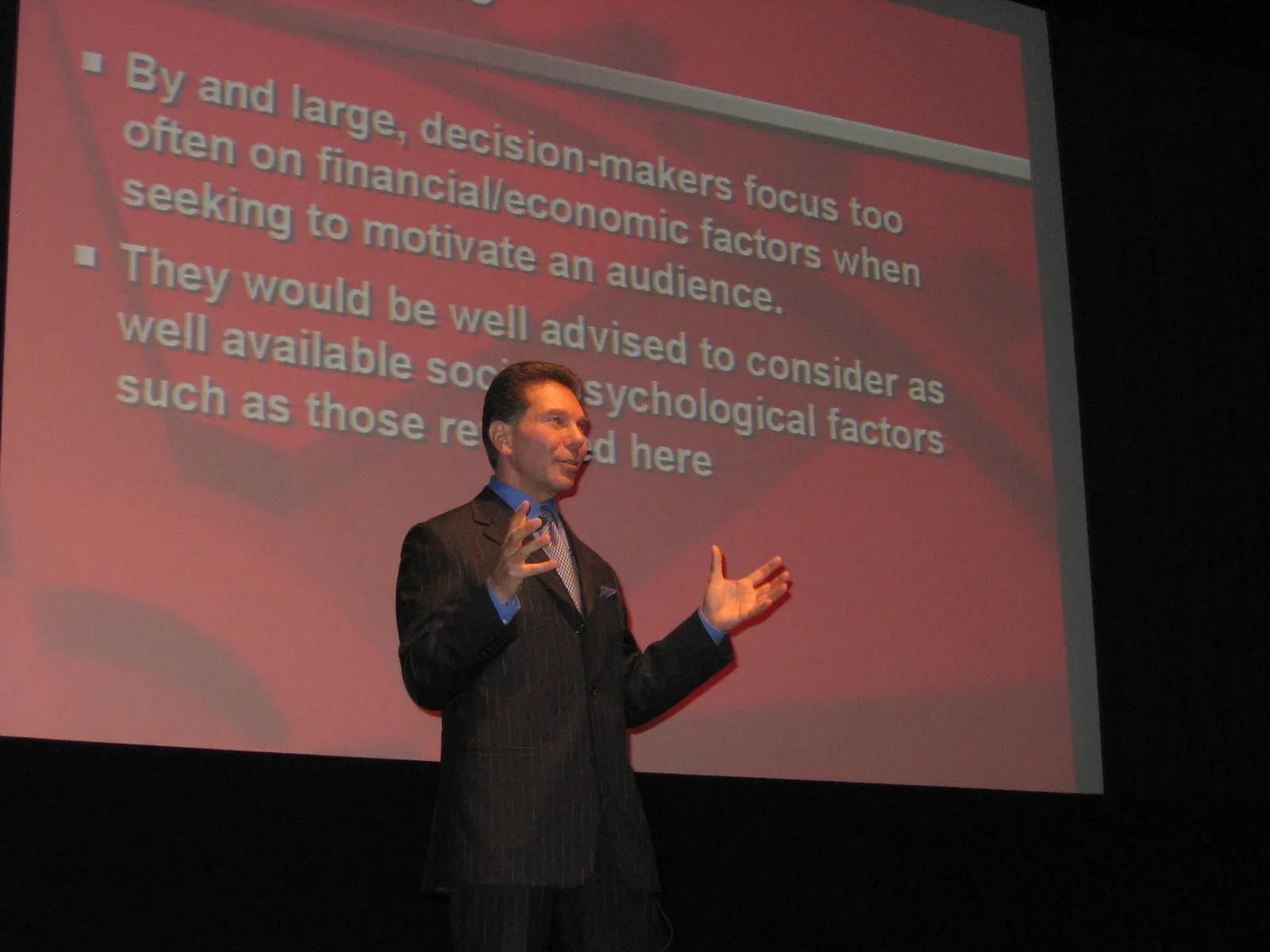 Dr. Robert Cialdini presenting a slide on the social and psychological factors that motivate an audience