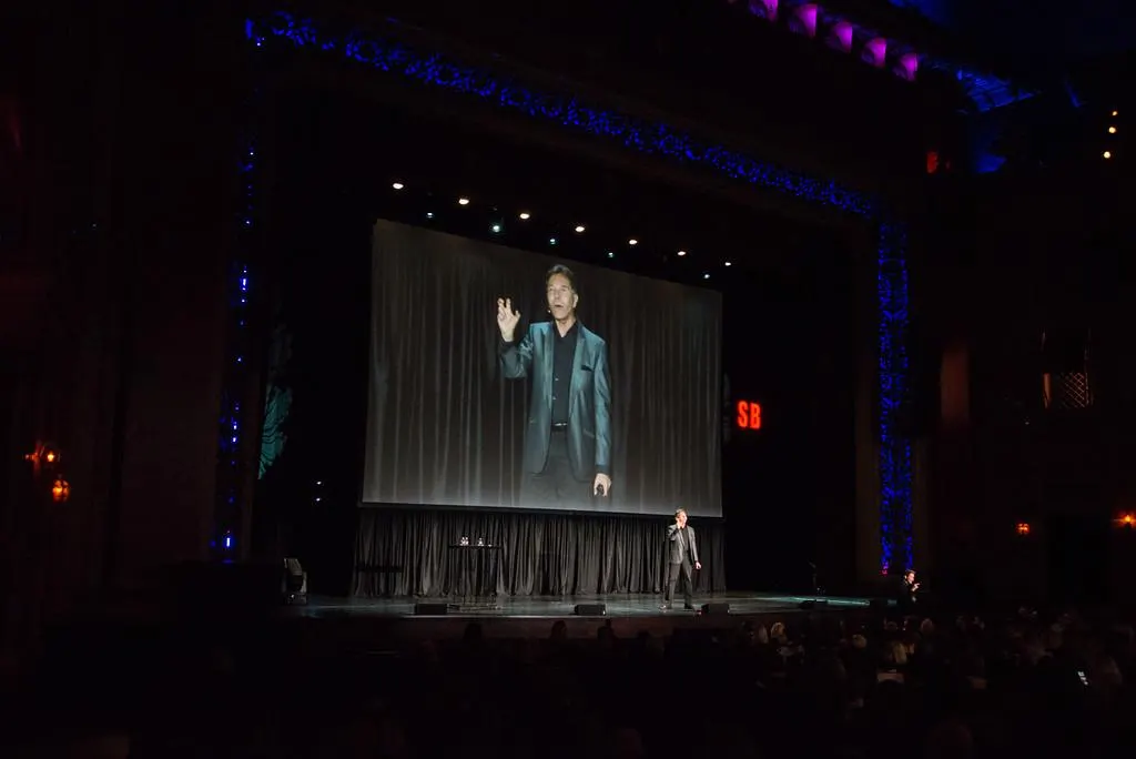 Dr. Robert Cialdini on a theatre stage, projected on the screen behind him