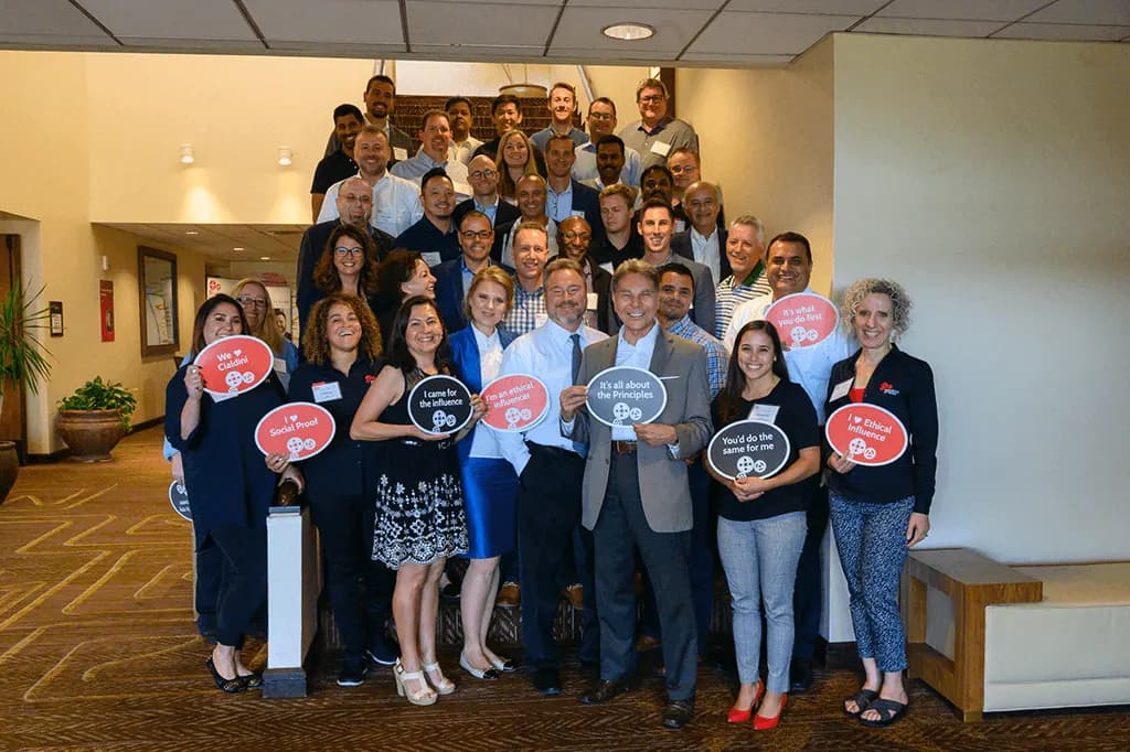 Dr. Robert Cialdini with a full workshop cohort holding signs about the principles